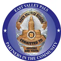 A circular badge logo with East Valley PALS at the top and Partners in the Community at the bottom. The center features an LAPD badge, North Hollywood Division, and Committed to Officers and Youth—promoting help and charity.
