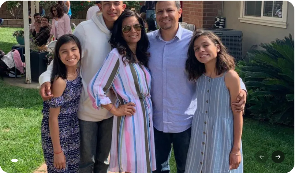 A family of five, including Claudia, stands together on the grass, smiling at the camera during their medical trip to Mexico. The sunny day captures three children and two adults with others in the background.